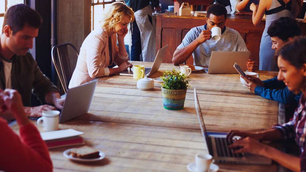 People sitting at a table in a coffee shop drinking coffee and looking at their laptops